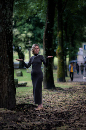 A woman stands calmly in a city park, surrounded by the natural beauty of tall trees.の写真素材