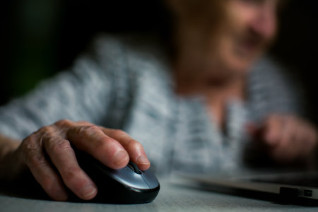 Close-up of an elderly woman's hand gently resting on a computer mouse while working with...