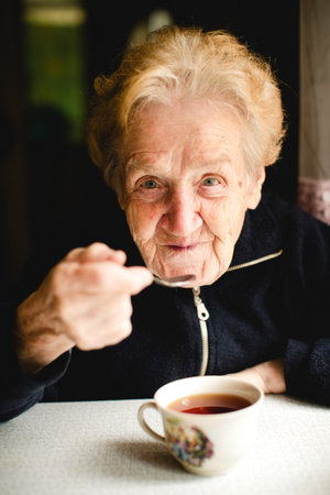 An elderly woman sits comfortably in her cozy home, enjoying a warm cup of tea.