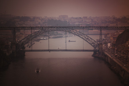 The Douro River and Dom Luis I Bridge enveloped in dense smoke from nearby wildfires, illuminated by the soft orange glow of the setting sun filtering through the haze.の写真素材