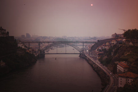 The Douro River and the Dom Luis I Bridge shrouded in thick smoke from wildfires, with the sun...
