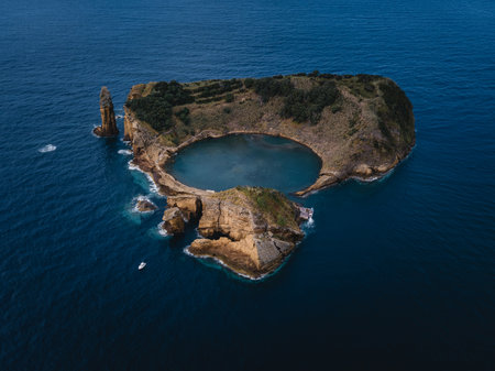 An aerial view of the Islet of Vila Franca do Campo, Azores, Portugal, showing its iconic circular lagoon surrounded by the Atlantic Ocean. The lush greenery contrasts beautifully with the deep blue waters, offering a stunning natural scene.の写真素材