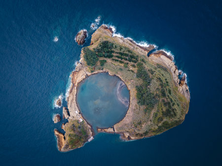 A vertical aerial view of the Islet of Vila Franca do Campo, Azores, Portugal, highlighting the circular lagoon surrounded by volcanic rock formations and the vast Atlantic Ocean.の写真素材