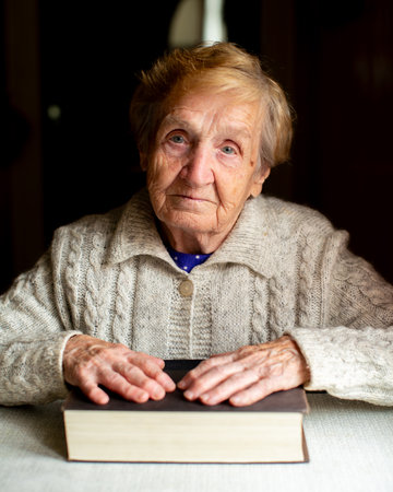 Portrait of an elderly woman stars sternly ahead, her hands resting on a thick book.の写真素材