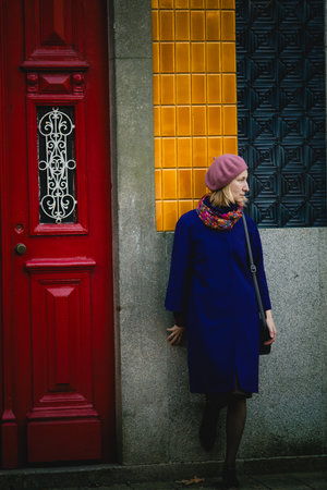 woman in a coat and neck scarf leans against the wall adorned with azulejos, with a thoughtful gaze on an autumn day.の写真素材