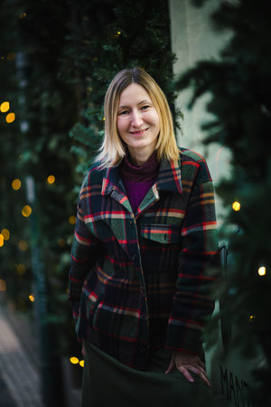 A portrait of a smiling woman in a checkered jacket, with festive fir branches and twinkling lights in the background, creating a warm holiday atmosphere.の写真素材