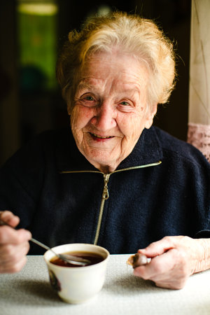 A cheerful elderly woman enjoys a cup of tea, her warm smile radiating positivity in this intimate portrait.の写真素材