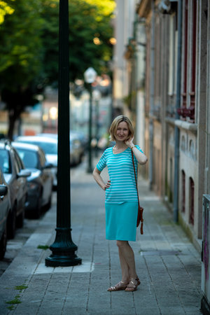 A woman in summer attire stands on a sidewalk in Portugal, exuding casual elegance and warmth.の写真素材