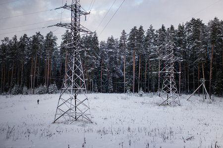 High-voltage power lines running through a snow-covered forest clearing, creating a stark contrast with the surrounding winter landscape.の写真素材