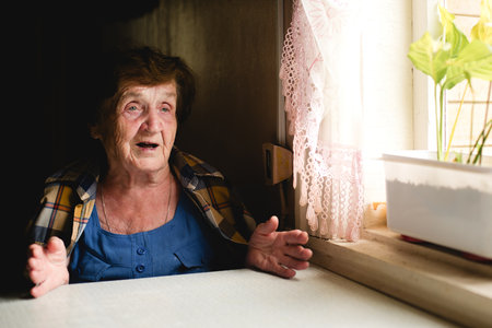 An elderly woman gestures expressively with her hands while talking, seated at a table in her home.の写真素材
