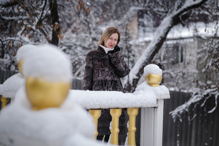 A blonde woman in a stylish fur coat stands in the snow during winter.の写真素材