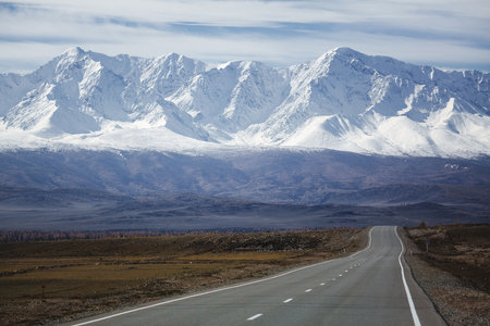 A road stretching into the distance toward the majestic North Chuysky Ridge with snow-capped peaks in the Altai Republic, creating a breathtaking and serene scene.の写真素材