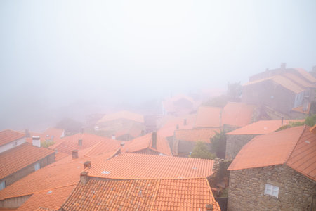 Terracotta rooftops in Monsanto, Portugal, disappearing into the mist on a foggy autumn day, creating a serene and mysterious atmosphere.の写真素材