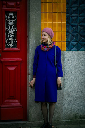 A woman in a stylish coat and beret standing near a traditional Portuguese city house, exuding elegance and charm.の写真素材