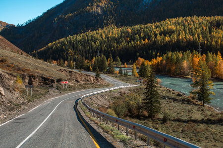 A zigzagging road through the Altai Republic with a river flowing on the right, surrounded by rugged mountains and lush wilderness.の写真素材