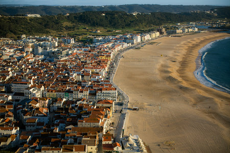 Aerial view of the beach and coastal rooftops in Nazare, Portugal, with a panoramic landscape on a calm and peaceful day.の写真素材