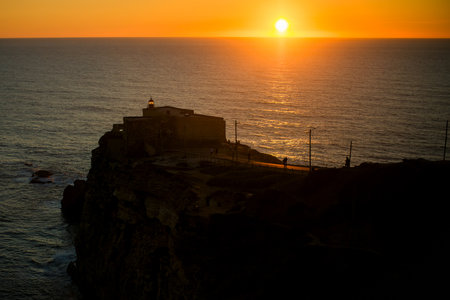 A lighthouse during sunset in NazarÃ©, Portugal, with vibrant colors painting the sky.の写真素材