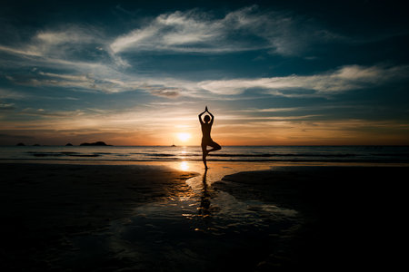 The silhouette of a woman practicing yoga on a tropical beach at twilight in Thailand, embracing meditation and serenity.の写真素材