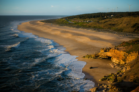 A sunlit beach in NazarÃ©, Portugal, on a clear day, with golden sands meeting the serene Atlantic Ocean under a bright blue sky.の写真素材