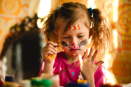 A little girl paints with bright colors, her face and hands covered in joyful smudges and brushstrokes. Creativity spills everywhere as she loses herself in the fun of making art.の写真素材