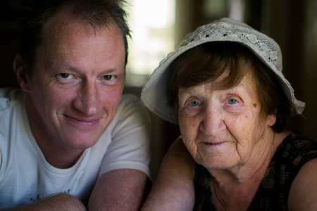 A close-up portrait of an elderly woman with her adult grandson. Their faces are close, showing a quiet bond and deep generational connection.の写真素材