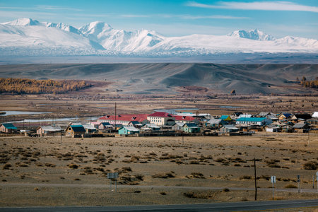 A small village in the Altai Republic near the border with Mongolia, surrounded by open land with snow-covered mountain peaks rising in the background. The scene feels remote, peaceful, and timeless.の写真素材
