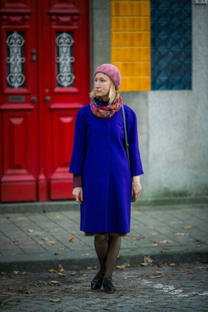 A woman in a cobalt blue coat and a beret stands in front of a red door and colorful tiled wall in Porto, Portugal. The scene feels vibrant, elegant, and quietly cinematic.の写真素材