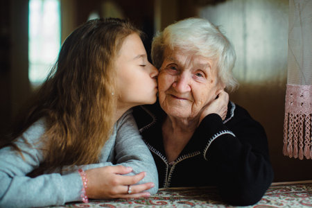 Young girl kissing an elderly woman on the cheek indoors, showing family affection and care, with soft natural light and a warm, intimate atmosphere.の写真素材