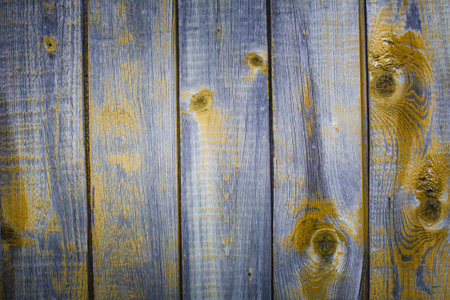 Close-up of weathered wooden boards with faded blue and yellow paint, highlighting grain, knots and...