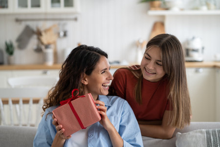 Laughing contented woman babysitter received gift from teenage girl stand near sofa in living roomの写真素材