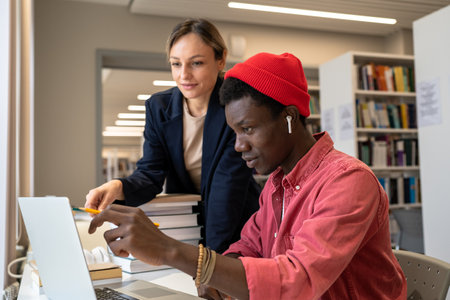 Personal tutor woman assisting puzzled focused student black guy in solve task at laptop in library.の写真素材