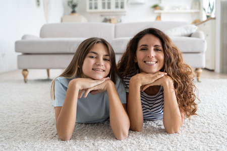 Charismatic cheerful woman and teen girl lying on floor with carpet posing for family photoの写真素材