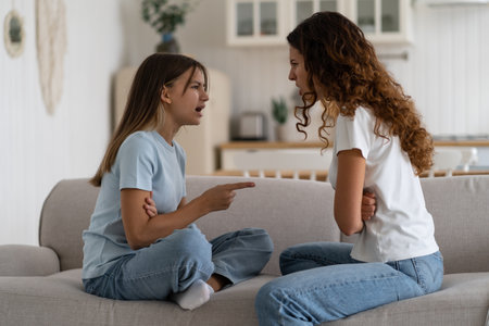 Emotional teen girl daughter fighting with mother at home, sitting in front of each other on sofaの写真素材