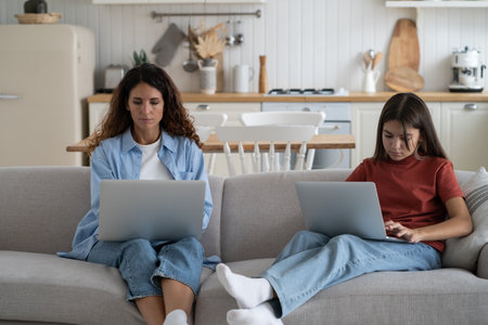 Mother and teen girl child sitting on sofa using laptops. Remote work and homeschoolingの写真素材