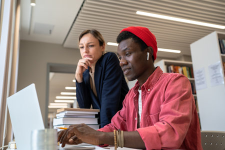 Two diverse students study partners learning together in library, using online databaseの写真素材