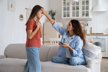 Unhealthy teen girl child complaining of sore throat to mother at home, kid got sickの写真素材