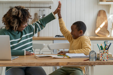 Pleased schoolboy and private tutor giving high five sit at home table celebrating success in studyの写真素材