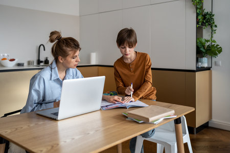 Working mom doing job on laptop and homework with son on kitchen at home.の写真素材