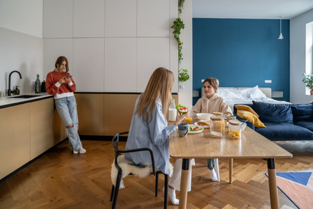 Teen girl using smartphone standing away of family having breakfast at kitchen table