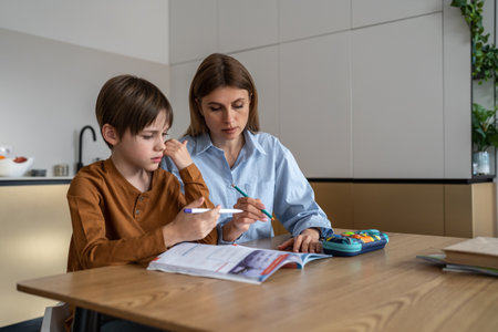 Caucasian mother and schoolboy son preparing school homework together at homeの写真素材