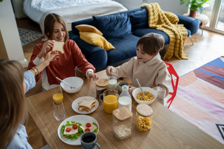 Happy smiling children brother and sister laughing while having breakfast with momの写真素材