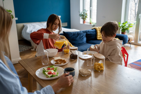 Mother and two kids sitting at kitchen table at home eating healthy food together in morningの写真素材