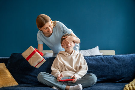Young happy loving mother closing eyes of child son congratulating little boy with birthday at homeの写真素材