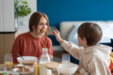 Happy kids siblings having fun together eating cereals in morning brother feeding sister corn flakesの写真素材