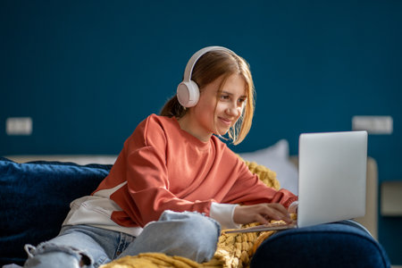 Smiling positive girl in headphones watching video movie on laptop sitting on couch.