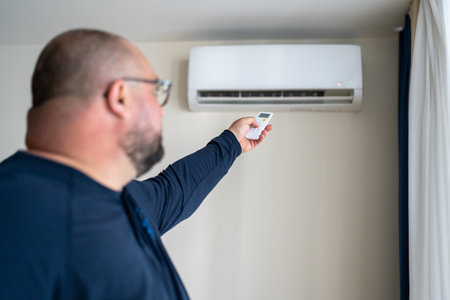 Overweight exhausted man using remote control to switch on air conditioner at home.の写真素材