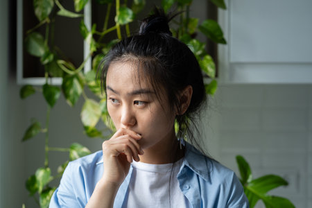 Thoughtful melancholic Asian woman touches lips with hand experiencing psychological disorderの写真素材