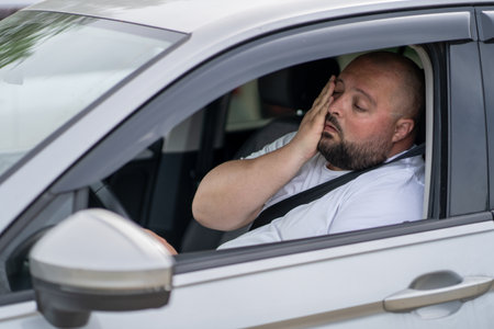 Tired overweight man drives car with broken air conditioner in hot summer weather.の写真素材