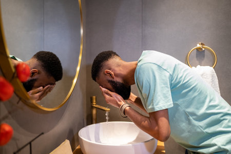 African American millennial guy cleaning skin in morning, washing face with water in bathroomの写真素材