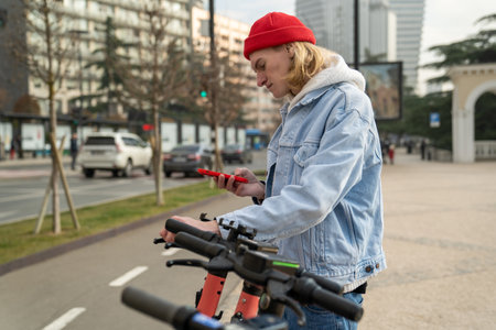 Hipster guy unlocking e-scooter with mobile phone outdoorsの写真素材
